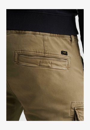 Nahaufnahme von Khaki-Hosen mit einer Gesäßtasche mit Paspel und einem kleinen schwarzen rechteckigen Markenetikett nahe der Taille, getragen mit einem schwarzen, gerippten Oberteil.