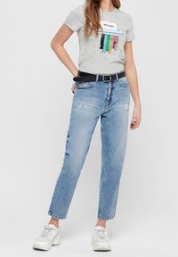 Svetle šedé tričko se textem "BAD VIBES" a barevnými pruhy, spárované se světle modrými roztrhanými rovnými džíny a bílými teniskami.