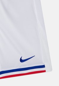 Camiseta deportiva blanca con logo de Nike en azul. Presenta franjas rojas y azules en el dobladillo. Está fabricada con material transpirable y acabado texturizado.