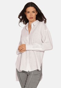 Weißes Leinenhemd mit Knopfverschluss, lockerer Passform, langen Ärmeln und abgerundetem Saum, kombiniert mit schwarz-weißen Gingham-Hosen.