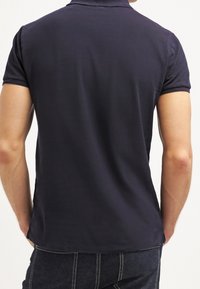 Marinblå polo med korta ärmar, platt krage och strukturväv. Har rak nederkant och en figursydd design.