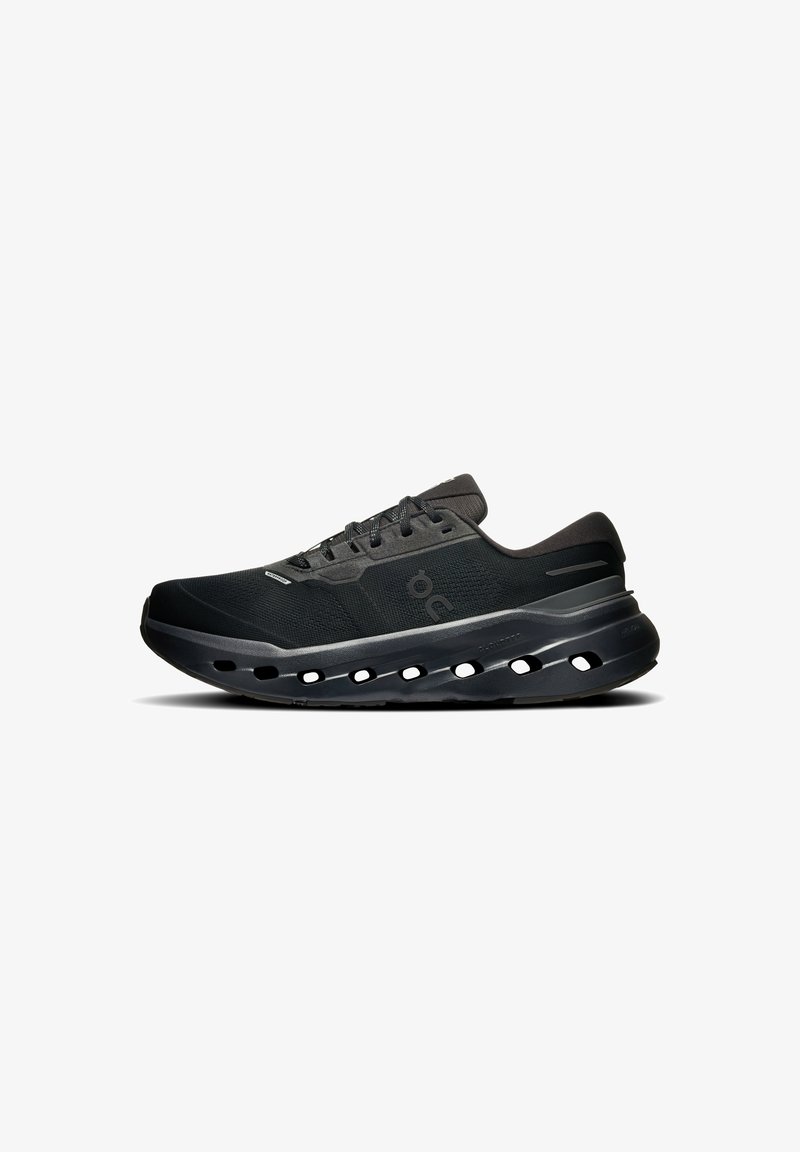 Baskets noires de sport avec tige en mesh, fermeture à lacets et semelle épaisse et rembourrée avec des trous de ventilation ovales sur le côté.