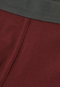 Maroon färgad bomullstyg med en texturerad yta, med en kontrasterande grå elastisk midjeband. Synliga sömmar längs kanterna.