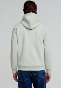 Lichtgroene hoodie met een gestructureerde afwerking, verstelbare capuchon en ribgebreide boorden, gecombineerd met blauwe jeans. De achterkant benadrukt het eenvoudige ontwerp.