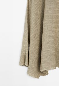 Tissu en lin beige drapé avec une texture de tissage diagonal visible et des plis doux sur un fond blanc uni.