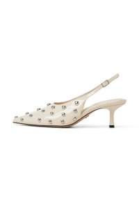 Kiilokärki slingback-korkokengät kiiltävässä kermanvärisessä patenttinanassa, joissa on terävä kärki, koristeltu hopeaisilla niiteillä ja hoikalla korolla.