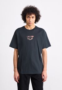 Sort bomulds T-shirt med korte ærmer, der har et centralt pink grafisk print, som inkluderer teksten "AIR max" og fem prikker nedenfor.