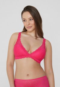 Růžový krajkový bralet s trojúhelníkovým tvarem, zvlněnými okraji a nastavitelnými ramínky, zdobený květinovými vzory a jemnou texturou.