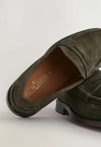 Groene suède instappers met een glad, rond voetbed, decoratieve stiksels en een contrasterende donkere zool. Voering aan de binnenkant in een warme bruin tint.