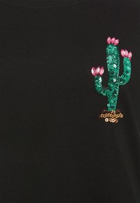 Sort stofskjorte med en grøn pailletkaktus med pink detaljer og en brun bund, der skaber et tekstureret, dekorativt design.