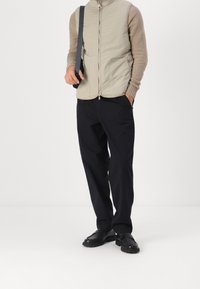 Padded beige vest with high collar, paired with dark wide-leg pants and black shoes, featuring a mix of textures in the top.