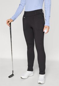 Juodos golf išties išsiskiriančios kelnes, pagamintas iš elastingos medžiagos, su dviem priekinėmis kišenėmis, vilkimos su šviesiai mėlynu ilgomis rankovėmis marškinėliais ir baltais batais.