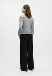 Grijze wollen trui met lange mouwen, getailleerd in de taille. Gecombineerd met zwarte, loose-fit gestreepte broeken. Eenvoudig ontwerp, gestructureerde stof.