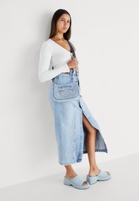 Jeans mini krilo s stranskim razporkom, združeno z oprijetim belim rebrastim topom. Dodatki vključujejo modro torbico na rami in svetlo modre klompe.