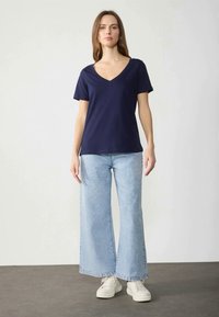 Marinblå V-ringad t-shirt med korta ärmar, kombinerad med vida ljusblå jeans. Jeansen har en urtvättad finish och en något fransad fåll.