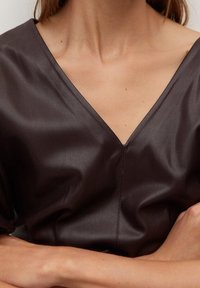 Blusa de cuero marrón con diseño de escote en V, mangas cortas y textura suave. Presenta un detalle de costura central.