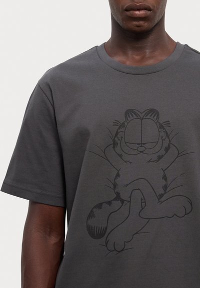 T-shirt en coton gris avec un graphique noir représentant un chat cartoon détendu, les yeux fermés et les bras levés, sur un fond uni.