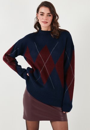 Temno modra in burgundska oversized pulover s diamantskimi vzorci, rebrastim ovratnikom in robom, v kombinaciji s prilegajočo burgundsko usnjeno krilo.