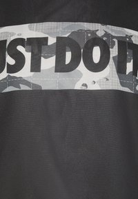 Primo piano di un tessuto nero con una striscia a camouflage grigia e bianca che presenta un audace testo nero parzialmente leggibile "FATTI".