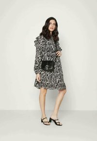 Vestido preto e branco com padrão, mangas com babados, cintura ajustada e saia até ao joelho. Combinado com uma pequena mala cruzada preta e sandálias.