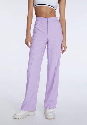 Mujer con pantalones lavanda de tiro alto y pierna ancha, zapatillas blancas de plataforma y un top corto blanco con rayas negras.