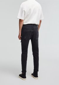 Vaqueros de mezclilla negra con un corte ajustado, con detalles desgastados y bolsillos traseros. Combinados con una camiseta de manga corta color crema y botas negras.