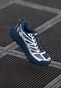 Baskets de course Hoka navy et blanches avec une semelle texturée, un design épuré et plusieurs lignes d'accent. Comprend un col rembourré et des lacets.