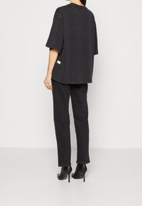 Camiseta negra de gran tamaño con mangas cortas, escote redondo y etiqueta lateral. Combinada con pantalones ajustados negros y zapatos de tacón alto.