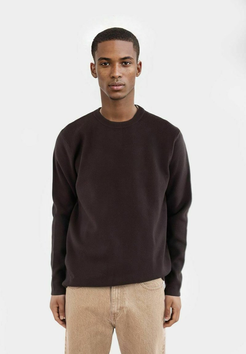 Svart sweatshirt med rund halsringning i texturerat tyg, med långa ärmar och avslappnad passform, tillsammans med beige denimbyxor.