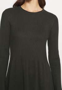 Abito in maglia a coste di un verde scuro, con maniche lunghe, scollo rotondo e orlo svasato con texture liscia.