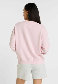 Sudadera rosa con corte oversized y hombros caídos, hecha de una tela suave, combinada con pantalones cortos de color gris claro. Diseño simple, sin patrones visibles.