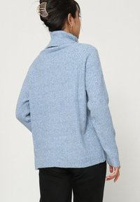 Pull col roulé côtelé bleu clair avec une coupe décontractée et des manches longues, présentant une texture subtile et un design à épaule tombante.