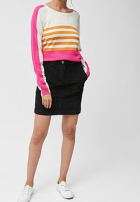 Strikket trøje med hvide, orange og lyserøde vandrette striber; stylet med en sort fløjlsnede nederdel og hvide sneakers.