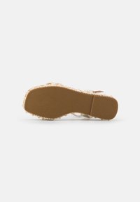 Sandal beige chiaro con suola in gomma testurizzata, caratterizzata da un design flat e dettagli di cinturino delicati. Accompagnata da accenti sottili.