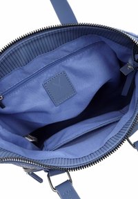 Blue handbag interior featuring a smooth fabric lining, zippered pocket, and multiple compartments. Includes a logo patch and rounded zipper.