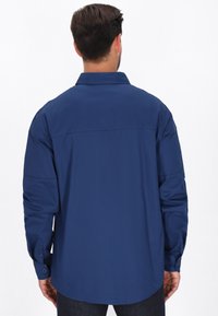 Camicia a maniche lunghe blu navy con colletto abbottonato, presenta un design a yoke, texture liscia ed è abbinata a jeans in denim scuro.