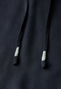 Tessuto di colore blu navy con una texture e piccole perforazioni, dotato di cordini scuri e accenti di un verde chiaro a contrasto alle estremità.
