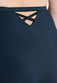 Close-up van marineblauwe stof met zwarte gekruiste banden over lichte huid bij een kleine driehoekige uitsnijding dicht bij de tailleband.