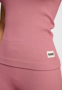 Débardeur rose côtelé à coupe ajustée, doté d'une petite étiquette rectangulaire avec l'inscription "hummel PERFORMANCE" sur l'ourlet inférieur.