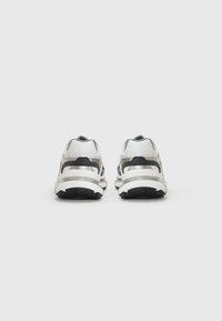 Pantofi sport albi, cu parte superioară din plasă și materiale sintetice, evidențiată de accente negre și o talpă groasă din cauciuc, având un design aerodinamic.