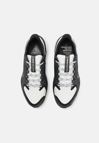 Black and white running shoes with mesh upper, textured detailing, reflective accents, and grey laces. Triangle logo on the tongue.