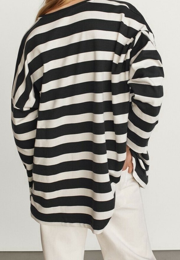 Maglietta a maniche lunghe oversize a righe bianche e nere con un fit rilassato, caratterizzata da un ampio scollo e cuciture delle spalle ribassate.