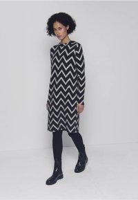 Abito a maniche lunghe con motivo a zigzag nero e crema, realizzato in tessuto strutturato, abbinato a stivali neri alla caviglia e leggings.