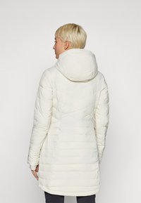 Hvid isoleret frakke med hætte, der har et kviltet mønster, lange ærmer og en skræddersyet silhuet. Glat tekstur og mellemlang design.