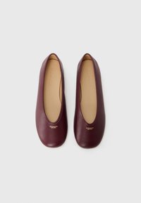 Ballerines en cuir bordeaux avec un bout rond, surface lisse et détail du logo doré sur le côté extérieur ; semelles intérieures beige doux.