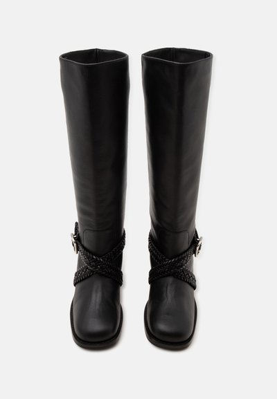 Paire de bottes en cuir noir hautes avec des bouts carrés et des lanières tressées croisées aux chevilles avec des boucles argentées.