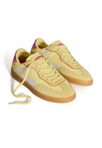 Zapatillas amarillas con parte superior de ante y tela, acentos en gris claro, logo rosa y suela de goma; cuenta con cordones planos y puntera redondeada.