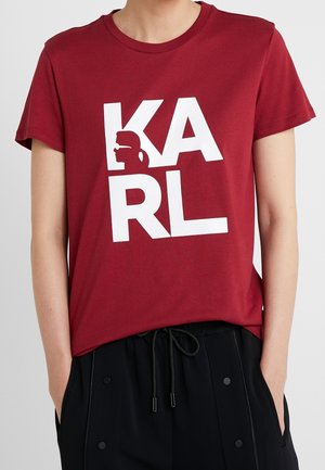 Person iført en rød t-shirt med fed hvid tekst "KARL" og en silhuet af en mand med solbriller inde i bogstavet "K".