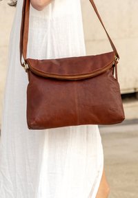 Brown leather shoulder bag with a zippered top, flat design, and smooth texture, featuring a long adjustable strap and visible stitching.