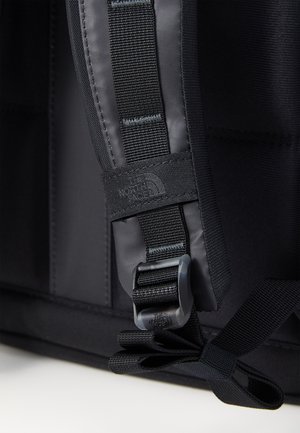 Gros plan sur la sangle noire d'un sac à dos avec boucle réglable et logo de la marque "The North Face" cousu sur la boucle en tissu.